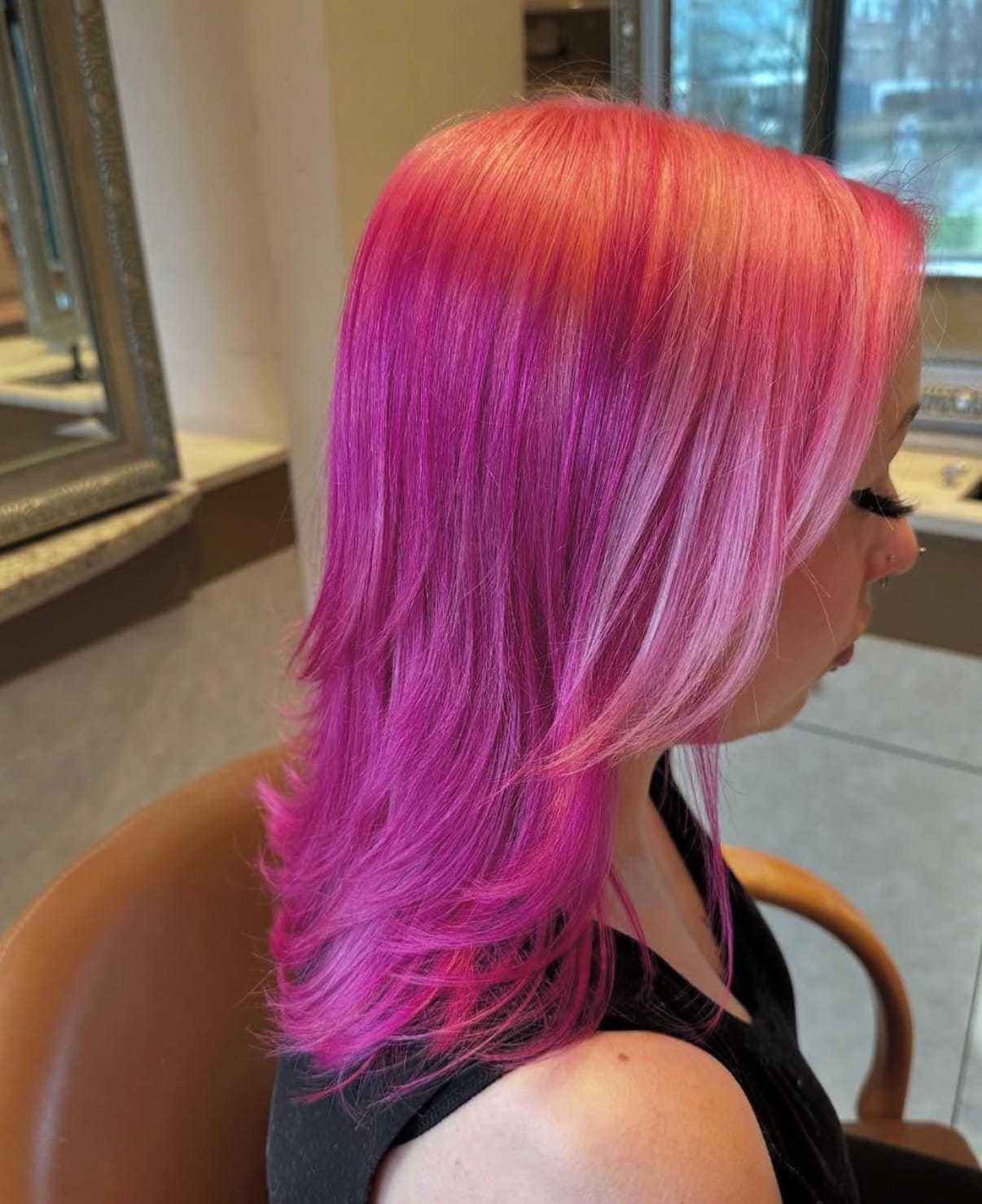 Side view of woman with bright pink layered hair in a salon setting.