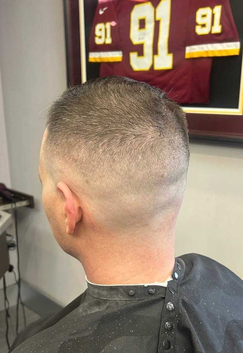 Buzz-cut hairstyle in a barbershop, with a framed sports jersey numbered 91 in the background.