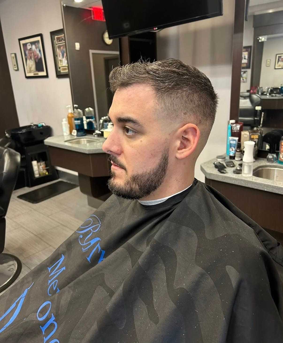 Man with a fresh haircut at a barbershop, sitting in a barber's chair, cape draped over him.