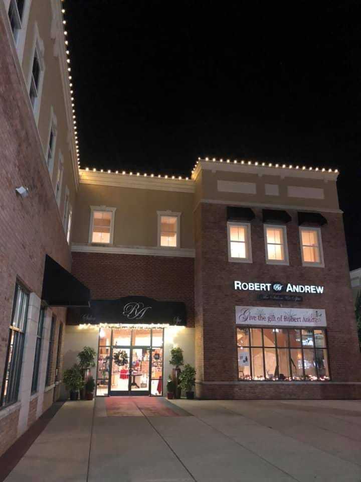 Illuminated storefront of "Robert Andrew" salon at night with decorated entrance and lit windows.