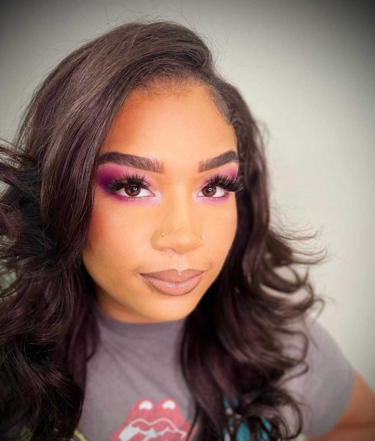 Woman with long hair and vibrant purple eye makeup wearing a graphic t-shirt.