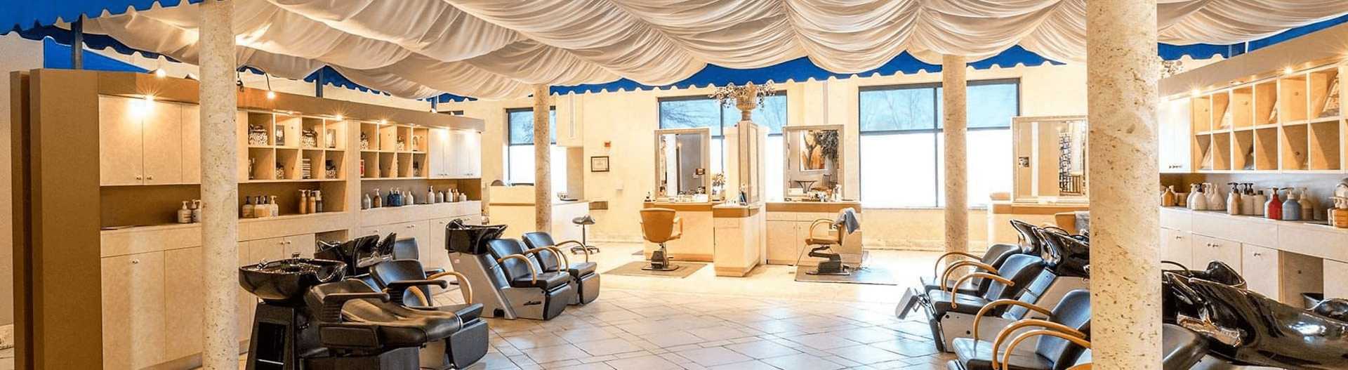 Luxurious hair salon with stylish chairs, wash stations, and elegant draped ceiling design.