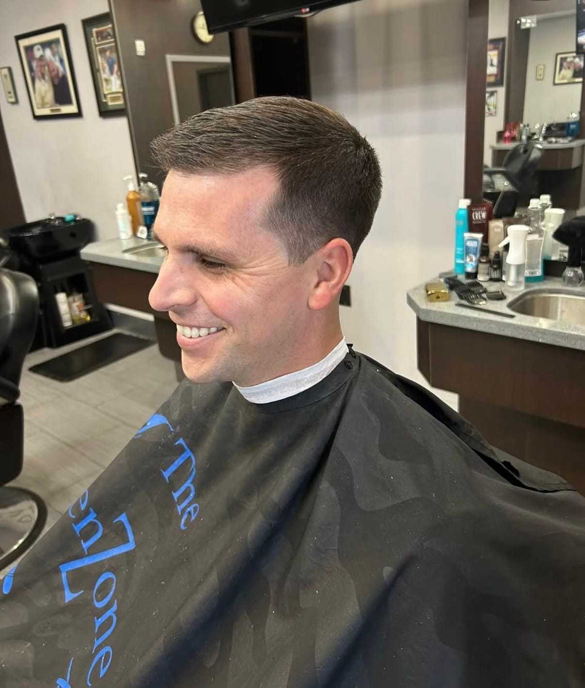 Smiling man with short haircut in a barbershop, surrounded by grooming products.