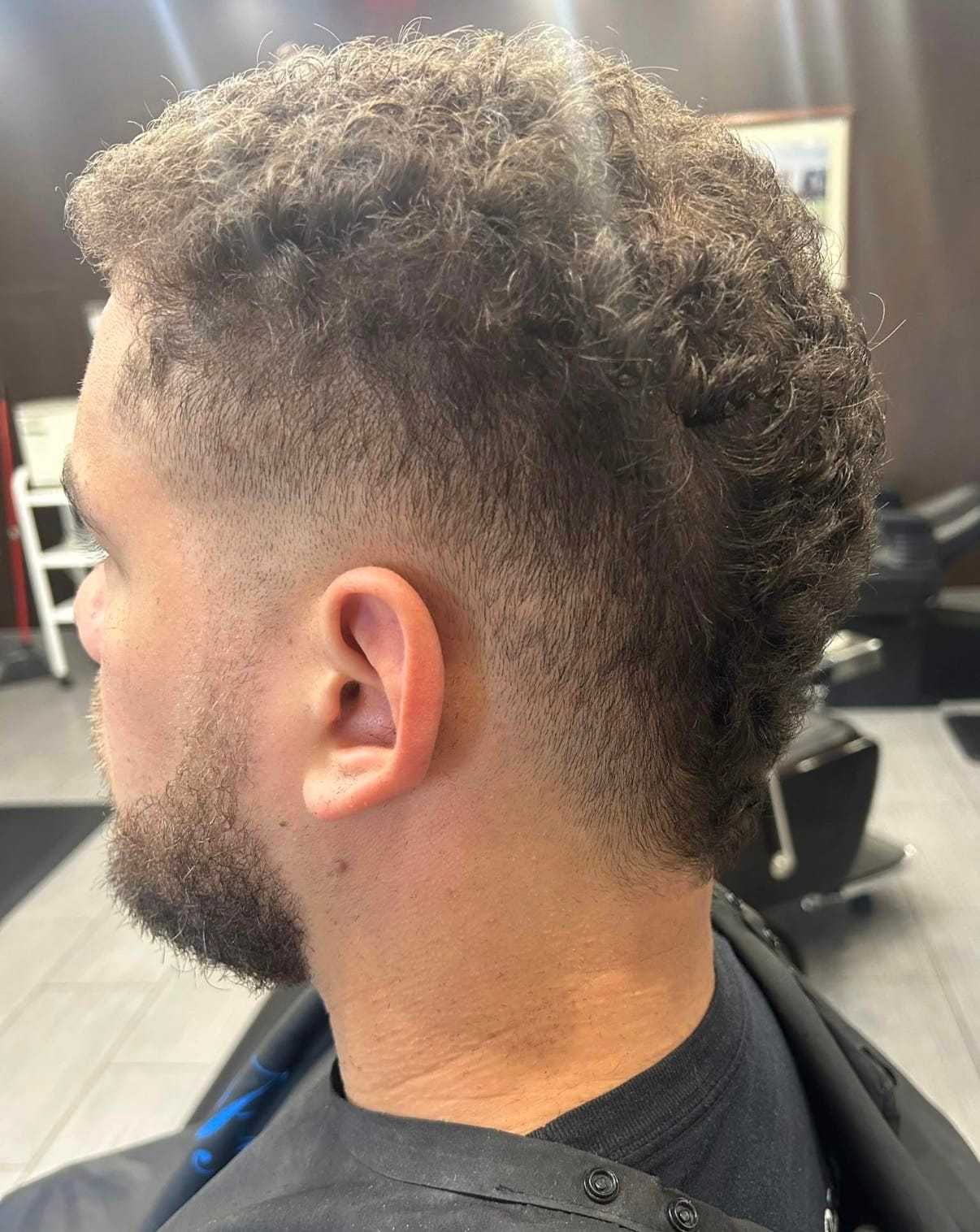 Side view of a man with a curly fade haircut in a barbershop setting.