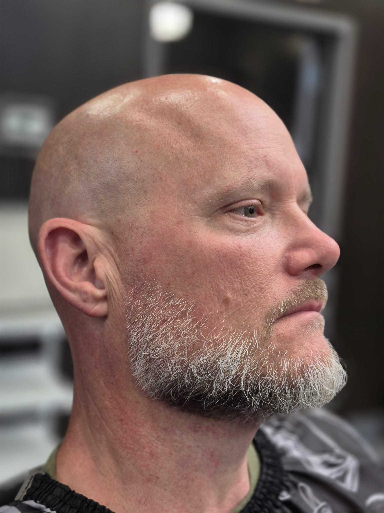 Man with a beard sitting in a barber chair, side profile.