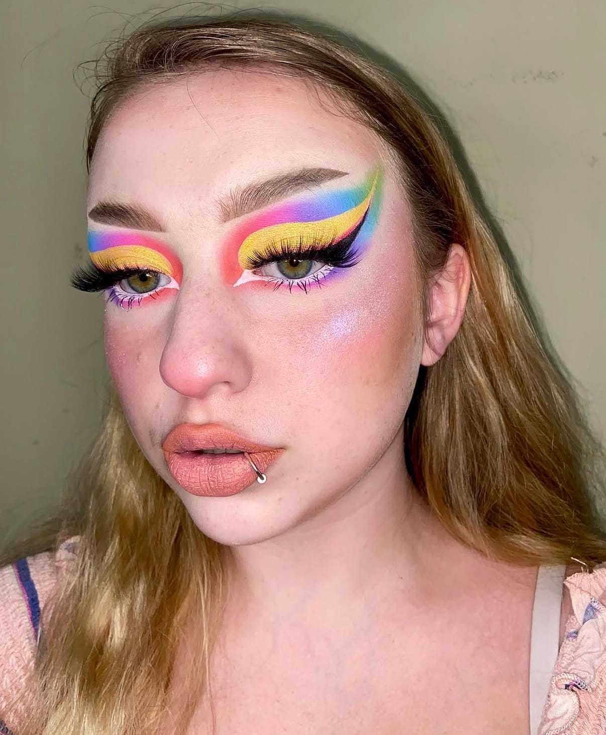 Bold rainbow eye makeup with dramatic eyeliner and long lashes.