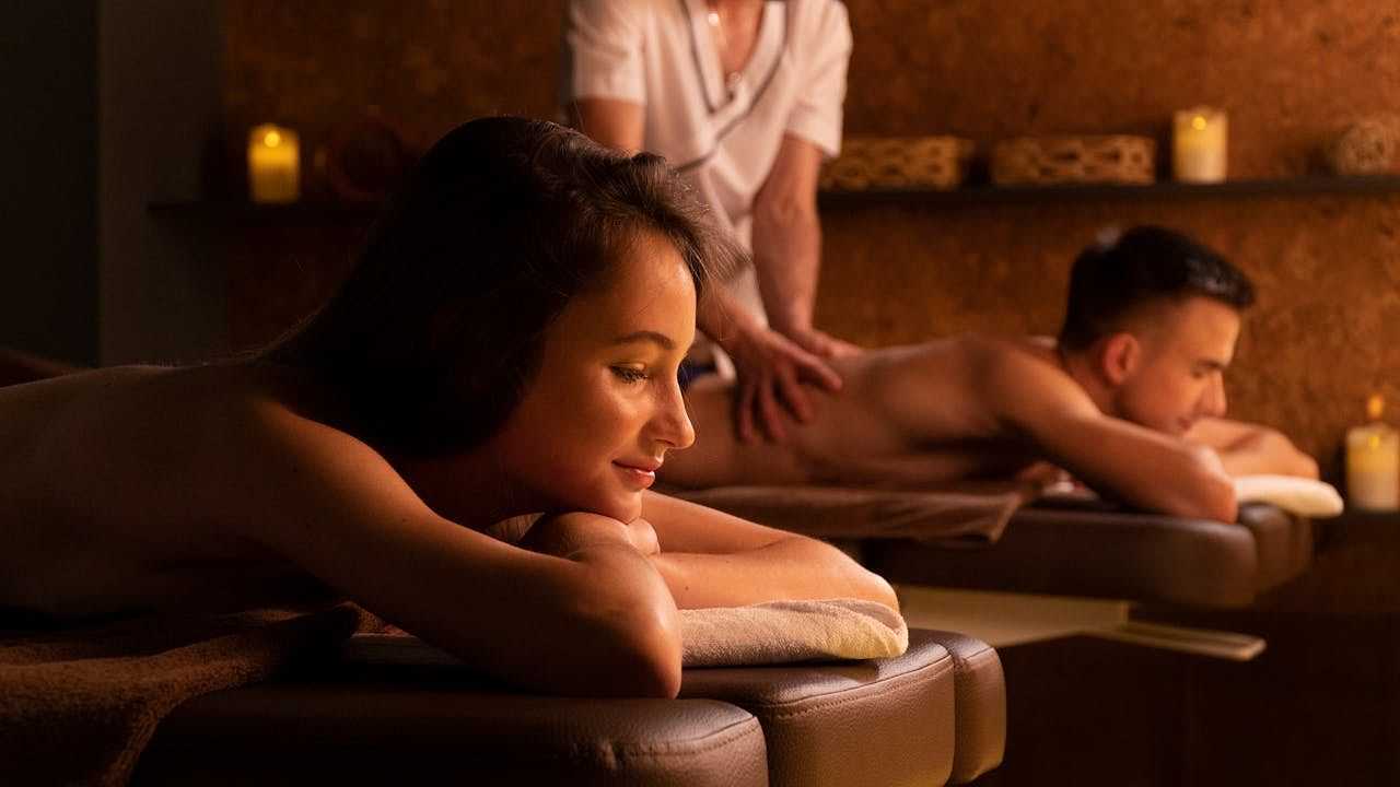 Couple enjoying relaxing back massages in a peaceful, candle-lit spa setting.